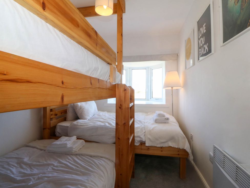 A bedroom with bunk beds a single bed a floor lamp and framed pictures on the wall at Ael Y Fron Aberdaron