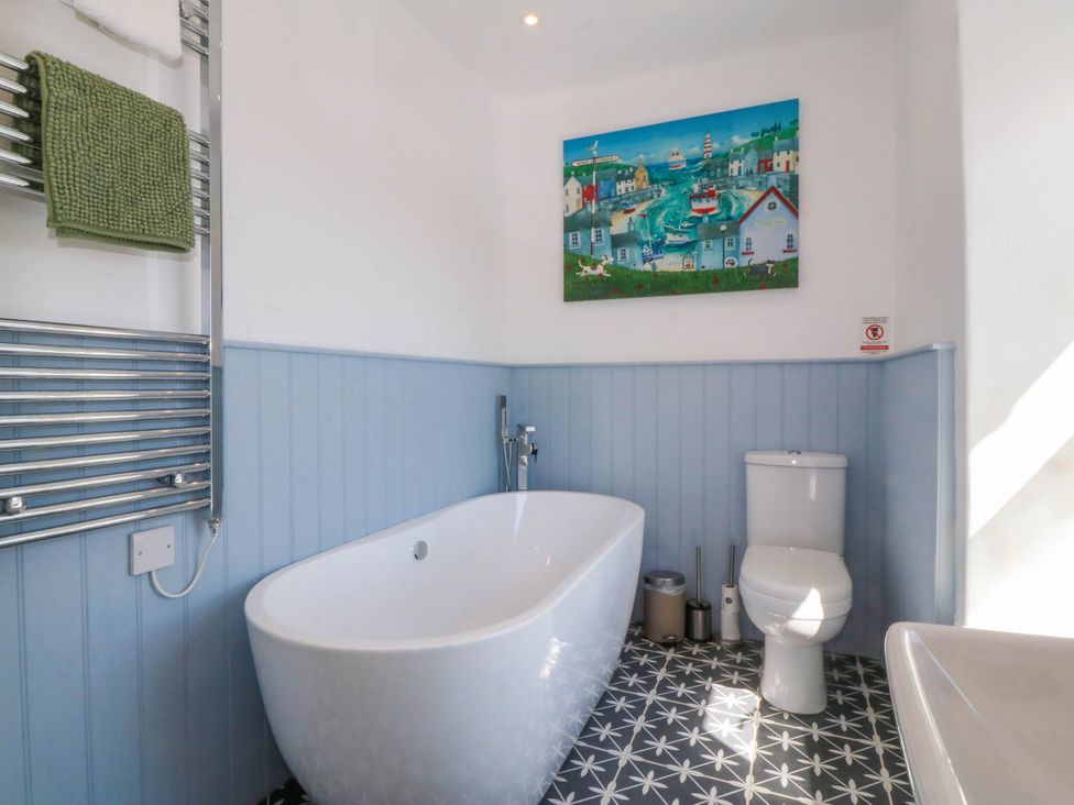 A bathroom with a white bathtub a toilet blue wall panels decorative floor tiles and a colorful painting at Ael Y Fron in Aberdaron