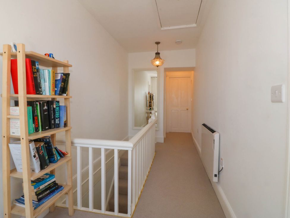A hallway with a bookshelf next to a staircase and a mirror on the wall at Ael Y Fron in Aberdaron