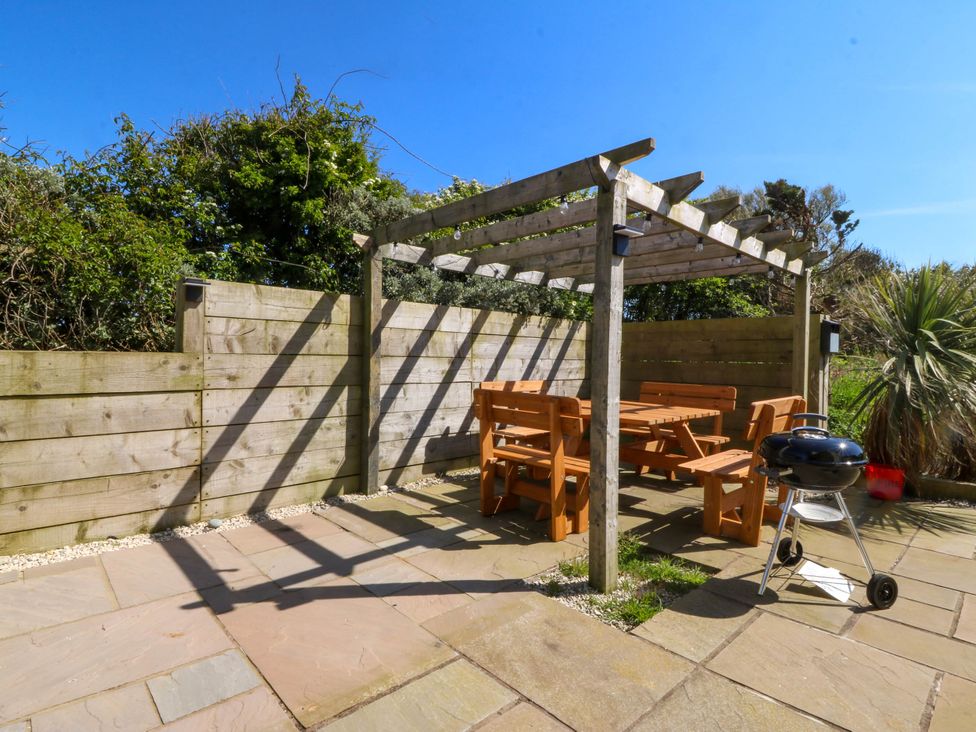 An outdoor patio area with wooden pergola wooden benches and table and a charcoal grill at Ael Y Fron in Aberdaron