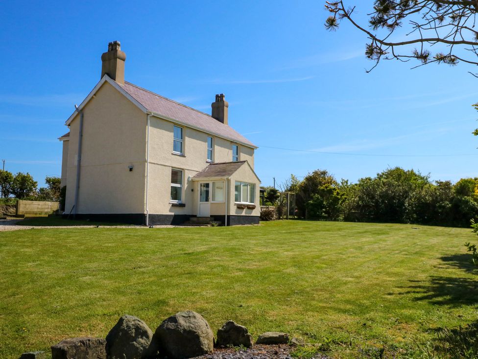 A two story house with two chimneys on a large lawn with trees in the background at Ael Y Fron in Aberdaron