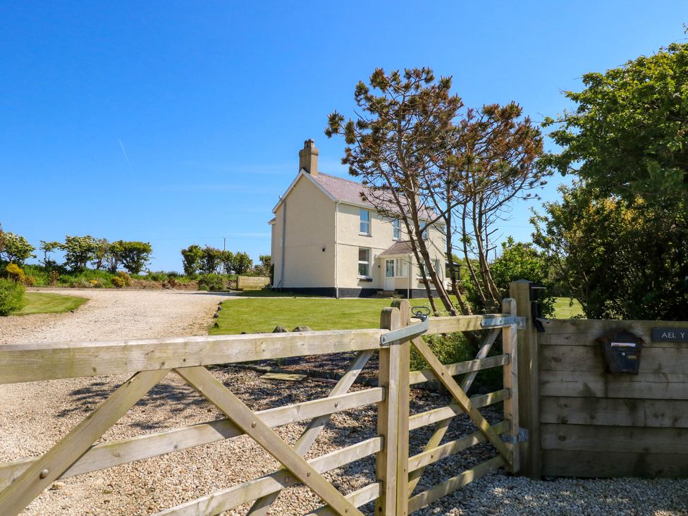 A detached house with a gravel driveway and wooden gate surrounded by grass and trees at Ael Y Fron in Aberdaron