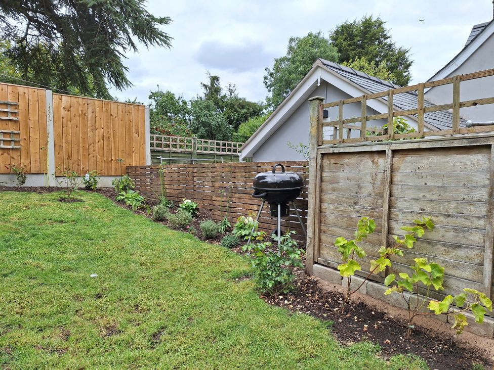 A garden with a barbecue and flower beds at Clematis Cottage in Minsterley