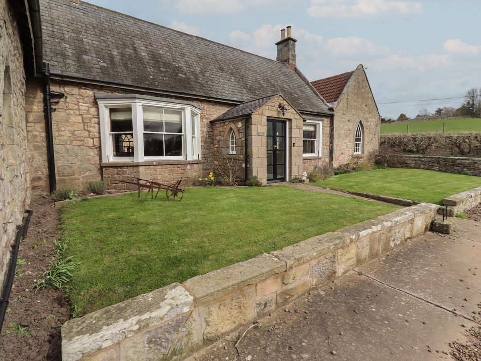 A garden with a stone wall and lawn at The Coach House in Crookham near Cornhill-On-Tweed