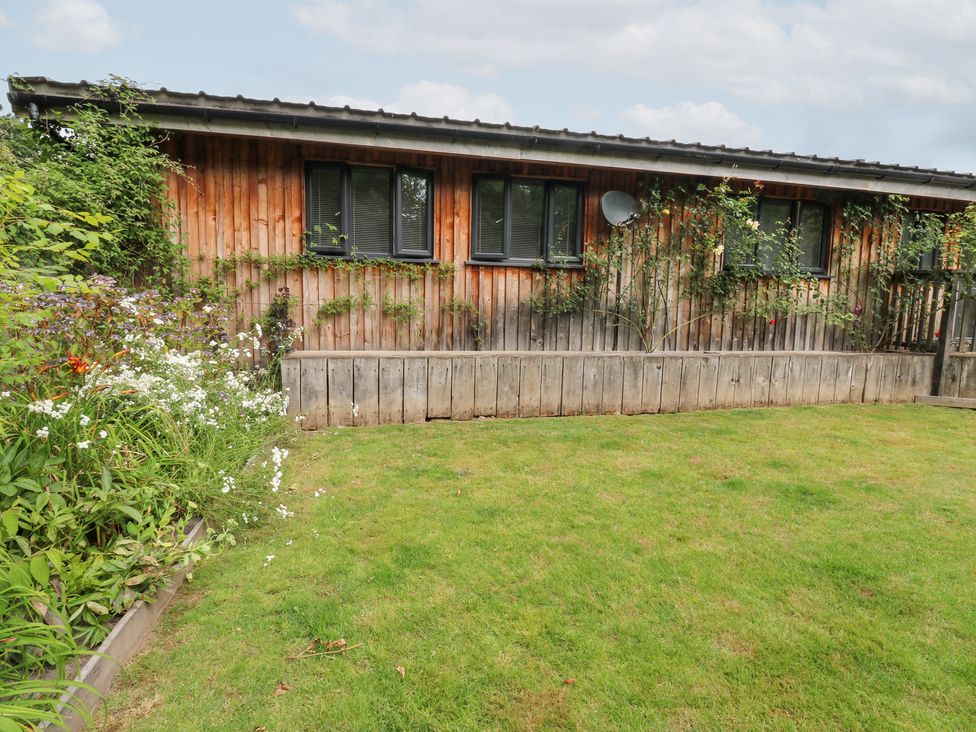 A garden with a wooden building and flower bed at Gloccamaura in Bovey Tracey
