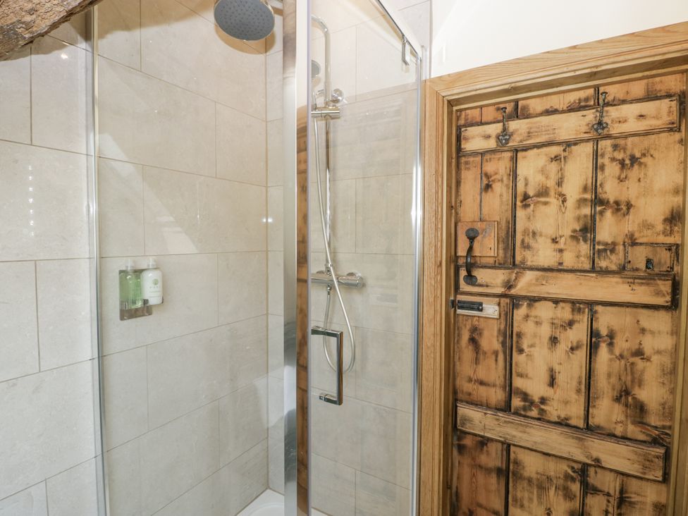 A shower with a glass enclosure and a wooden door at Evenjobb Court Farmhouse Evenjobb near Presteigne