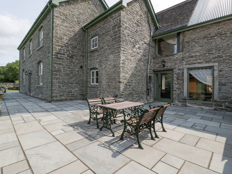 An outdoor patio with a stone wall and furniture at Evenjobb Court Farmhouse Evenjobb near Presteigne