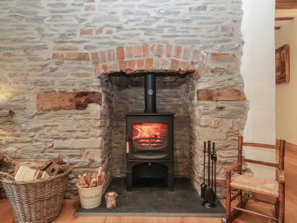 A living room with a wood burning stove and logs at Evenjobb Court Farmhouse Evenjobb near Presteigne