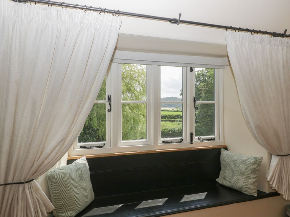 A window with curtains and a cushion on the windowsill at Evenjobb Court Farmhouse in Evenjobb near Presteigne
