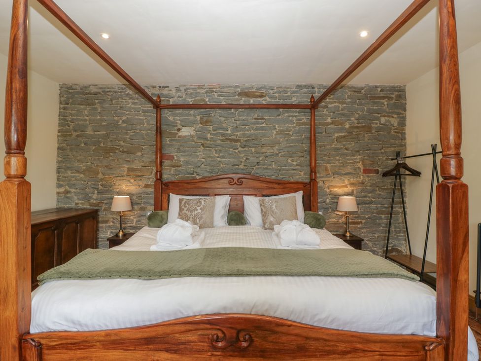 A bedroom with a four-poster bed and stone walls at Evenjobb Court Farmhouse near Presteigne