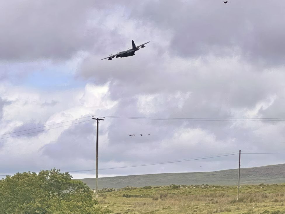 An aircraft flying near an electric pole and birds in the sky at Ty Drws Nesaf Cwmllynfell
