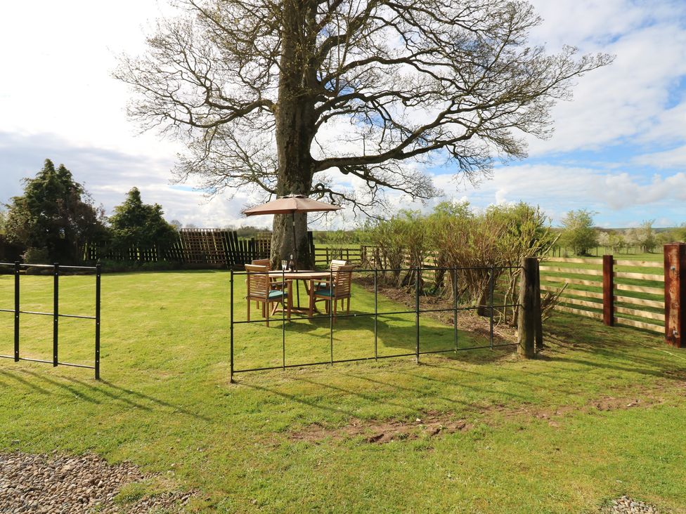 A garden with a table and chairs under a parasol at Rainbow Cottage in Kirkby Stephen