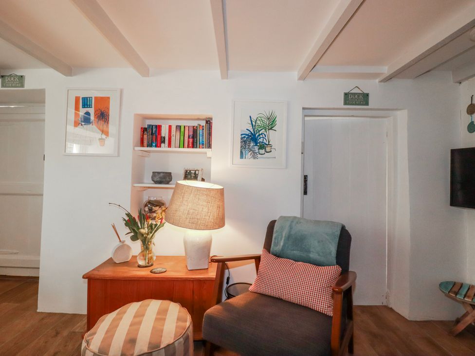 A living room with a lamp and bookshelf at Ivy Cottage in Trenale near Tintagel