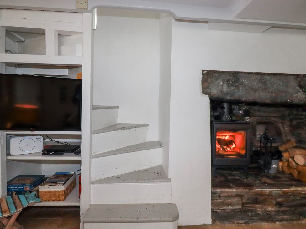 A living room with a staircase and a fireplace at Ivy Cottage in Trenale near Tintagel