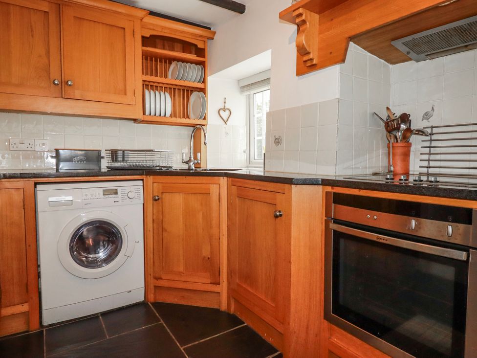 A kitchen with wooden cabinets and appliances at Ivy Cottage in Trenale near Tintagel