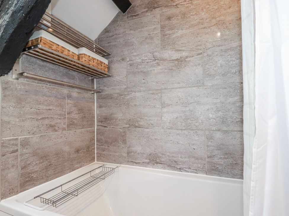 A bathroom with a bathtub and shelves in Ivy Cottage Trenale near Tintagel