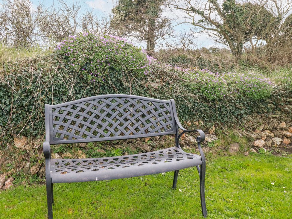 A bench on grass surrounded by bushes at Ivy Cottage in Trenale near Tintagel