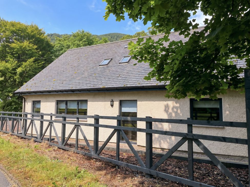 A house with a fence and trees at Nevis Bridge House in Fort William