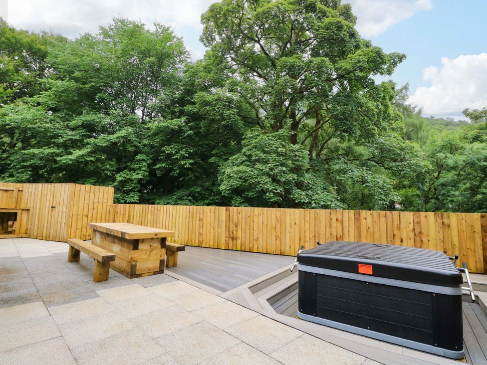 An outdoor deck with a wooden table and hot tub at Nevis Bridge House in Fort William