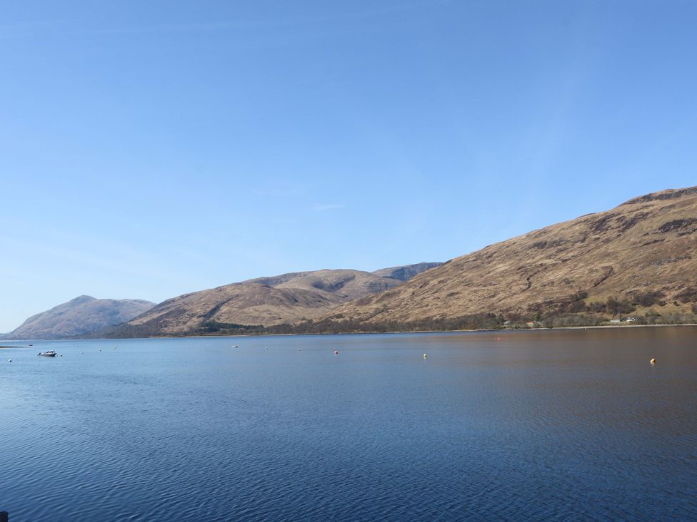 A lake with mountains and a boat at Nevis Bridge House in Fort William