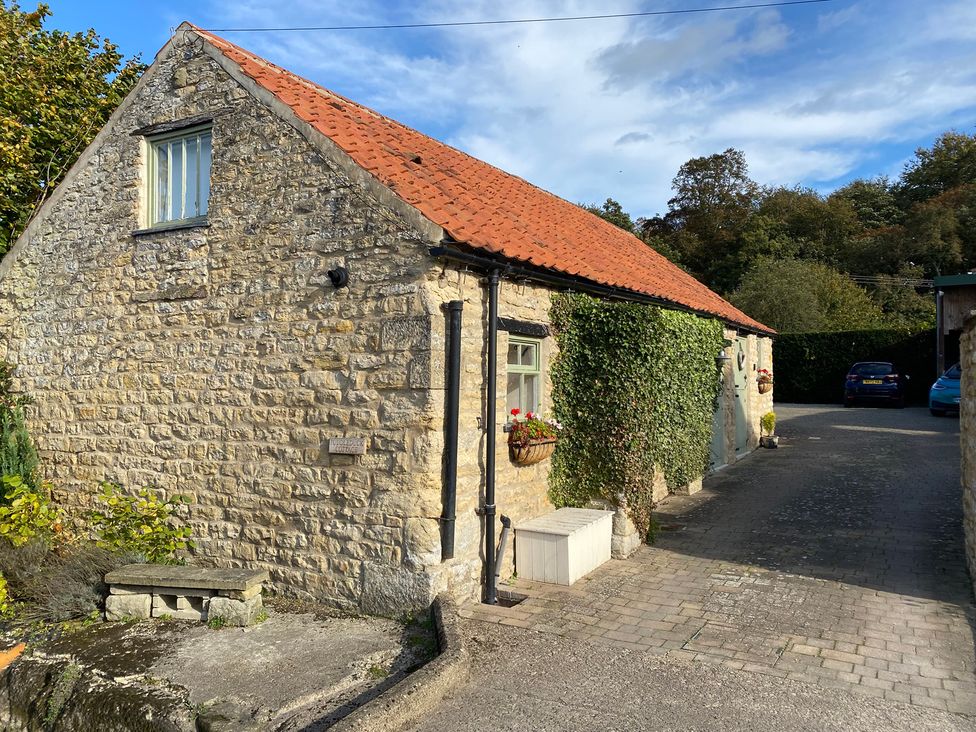 A stone cottage with a red roof and foliage near a parking area at Puddleduck Cottage in Thornton-Le-Dale