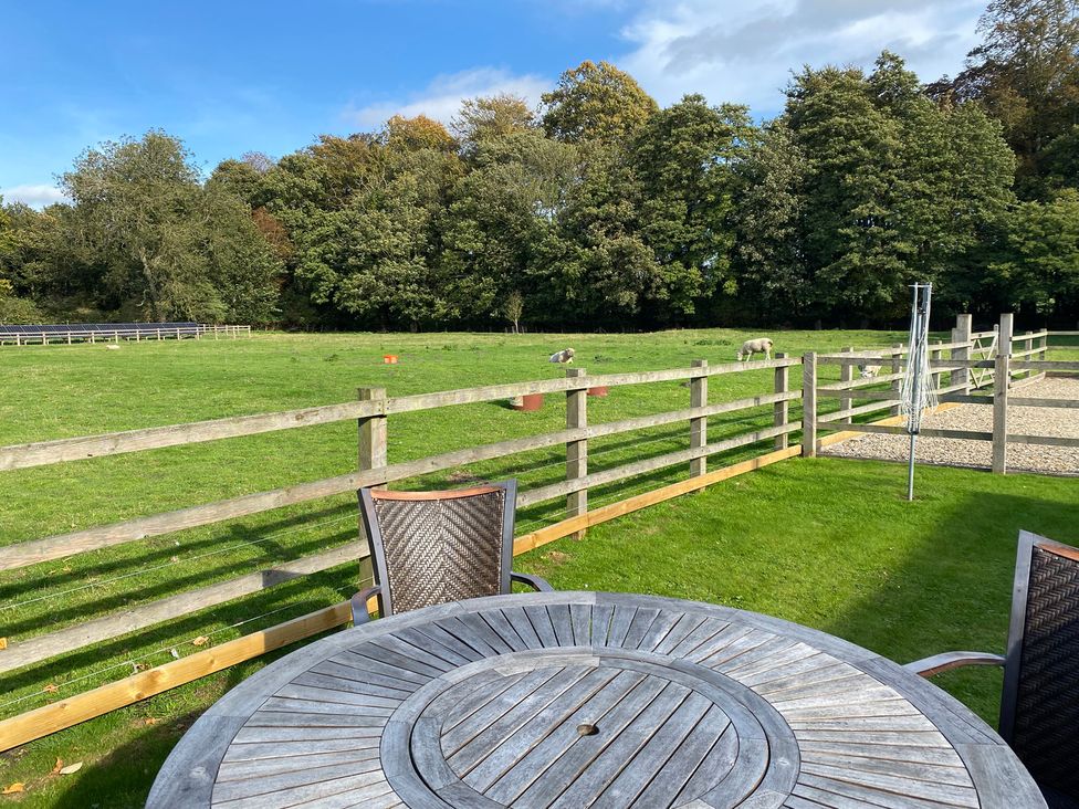 A garden with a wooden table and chairs overlooking a field with sheep at Puddleduck Cottage in Thornton-Le-Dale