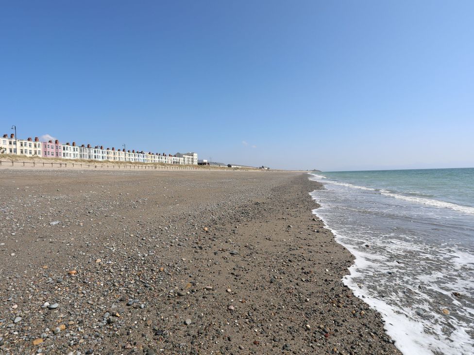 A beach with a sea lapping at the shore and buildings in the background at Bryn Caled Llanarmon near Y Ffor