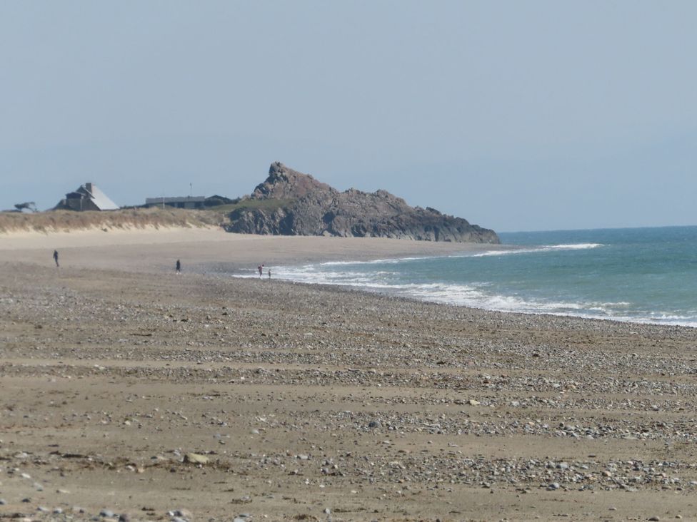 A beach with people in the distance and rocks at Bryn Caled Llanarmon near Y Ffor