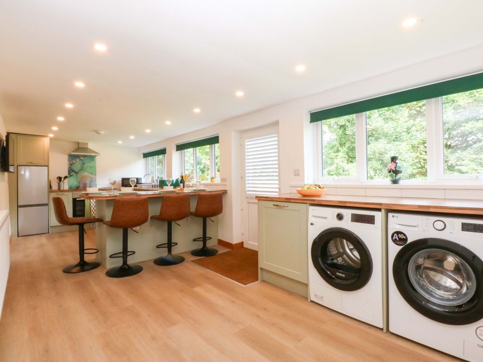 A kitchen with bar stools and washing machine at Cromlech Cottage at Cromlech Manor Farm near Benllech