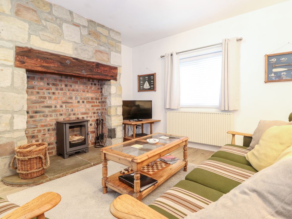 A living room with a stone and brick fireplace a wood stove a wooden coffee table and a striped sofa at Canny Cottage Low Hauxley Nr Amble