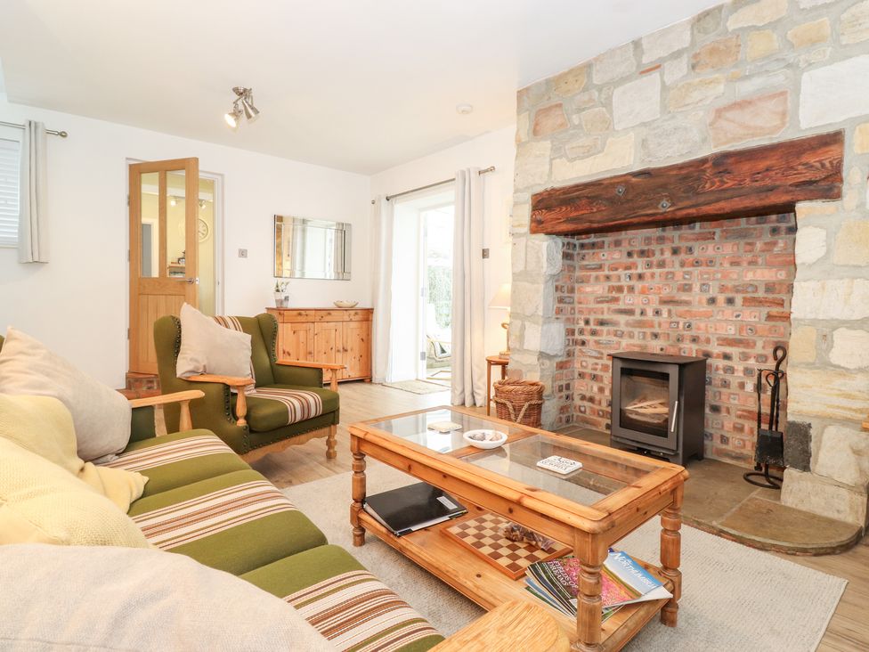 A living room with an armchair and sofa facing a stone fireplace with a wood stove at Canny Cottage Low Hauxley Nr Amble