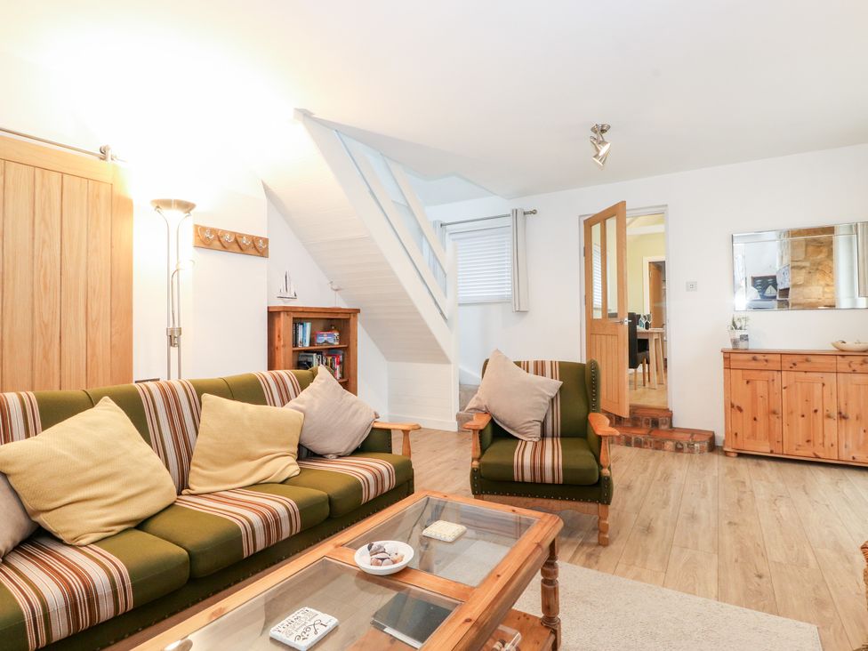 A sitting room with a striped green sofa and armchair a wooden coffee table a wooden sideboard and a bookshelf at Canny Cottage Low Hauxley Nr Amble
