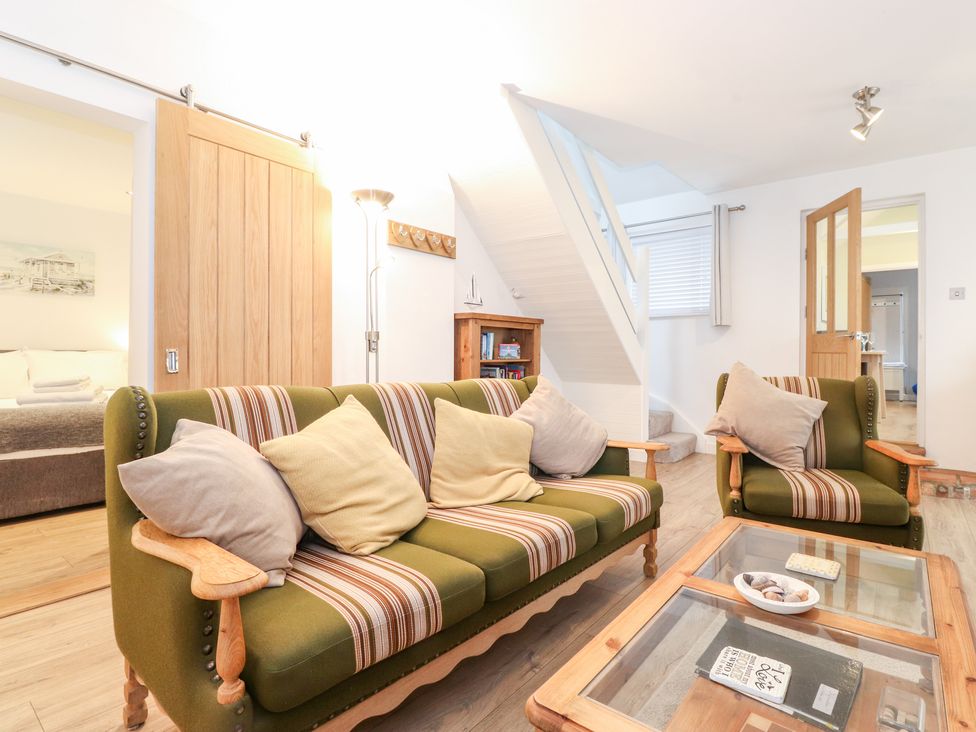A living room with green striped sofas, a glass coffee table, wooden doors, a staircase, and a bookshelf at Canny Cottage Low Hauxley Nr Amble