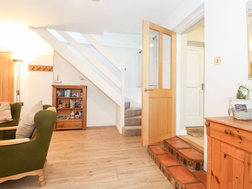A living room with green armchairs wooden bookshelf and staircase at Canny Cottage in Low Hauxley Nr Amble
