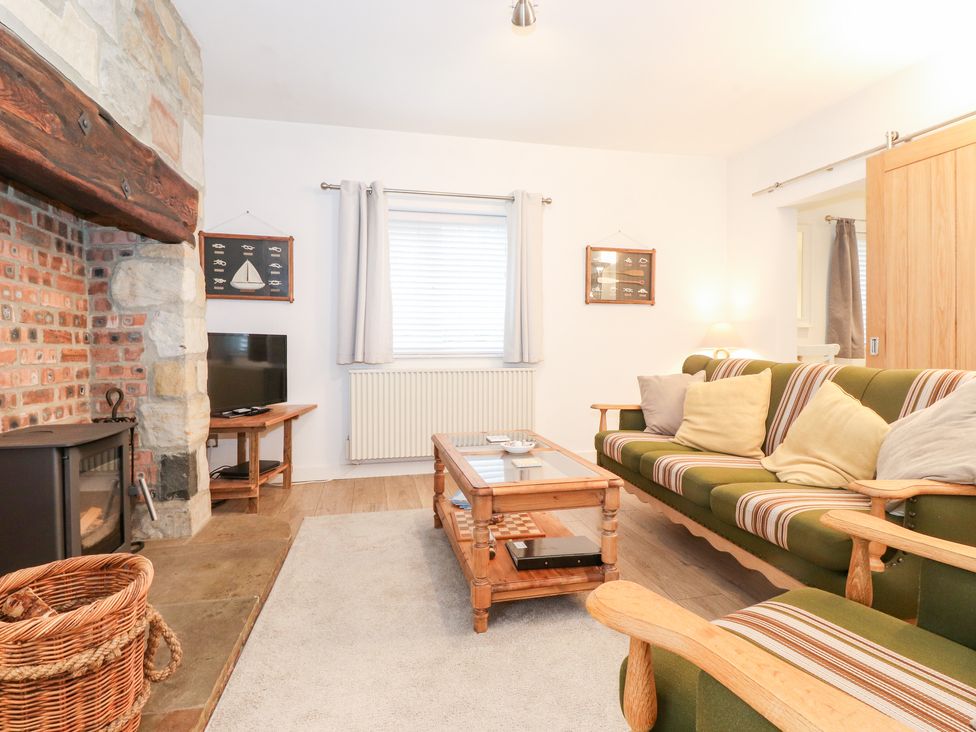 A living room with a fireplace television green striped sofa wooden coffee table and wicker basket at Canny Cottage Low Hauxley Nr Amble