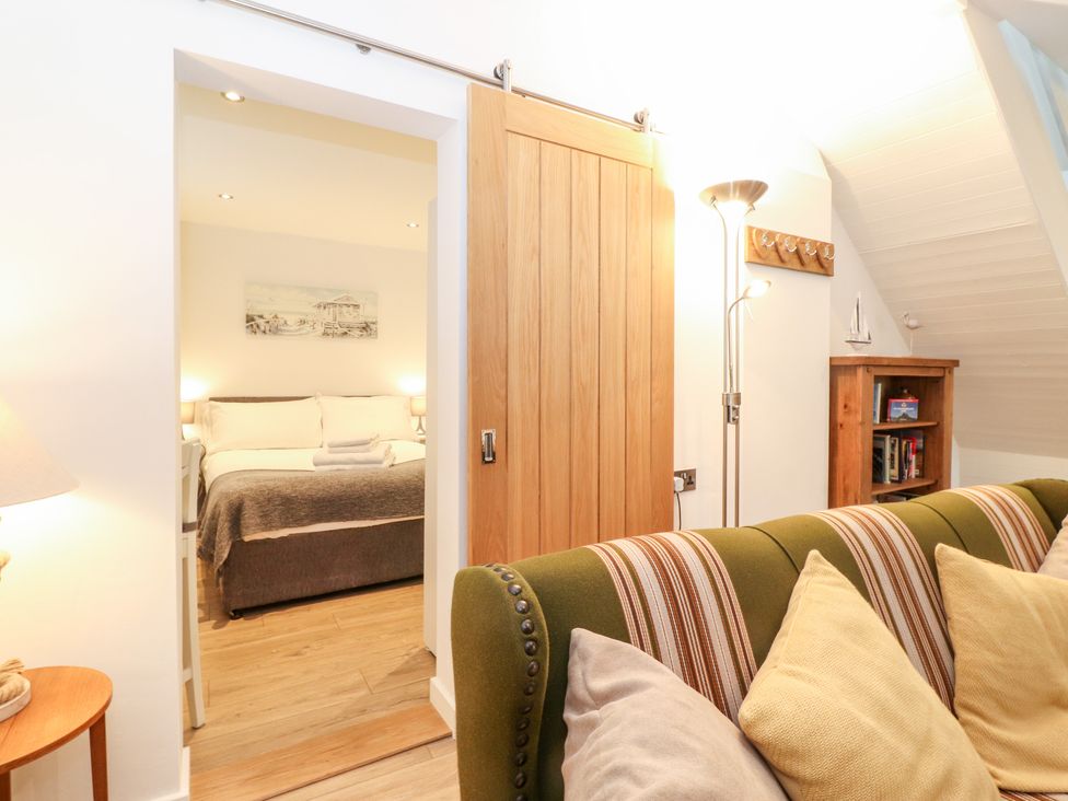 A seating area with a green striped couch and pillows next to a wooden sliding door leading to a bedroom with a bed and folded towels at Canny Cottage Low Hauxley Nr Amble