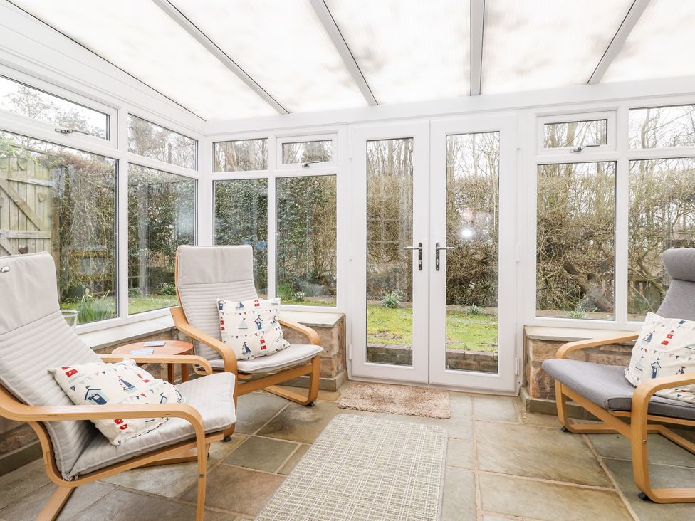 A conservatory with three armchairs a small round table and glass doors overlooking a garden at Canny Cottage Low Hauxley Nr Amble