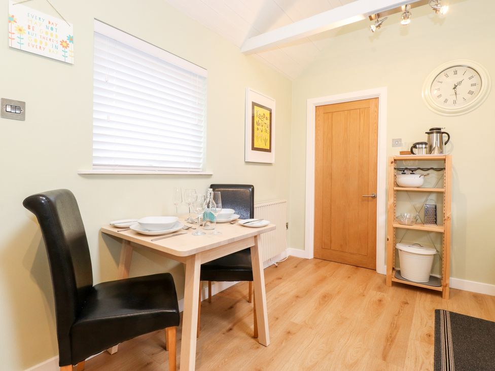 A dining area with a small wooden table set for four with two black chairs a wooden door and a wooden shelving unit with kitchen items at Canny Cottage Low Hauxley Nr Amble