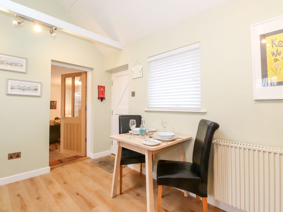 A dining area with a small wooden table set for two black chairs and a window with blinds at Canny Cottage Low Hauxley Nr Amble