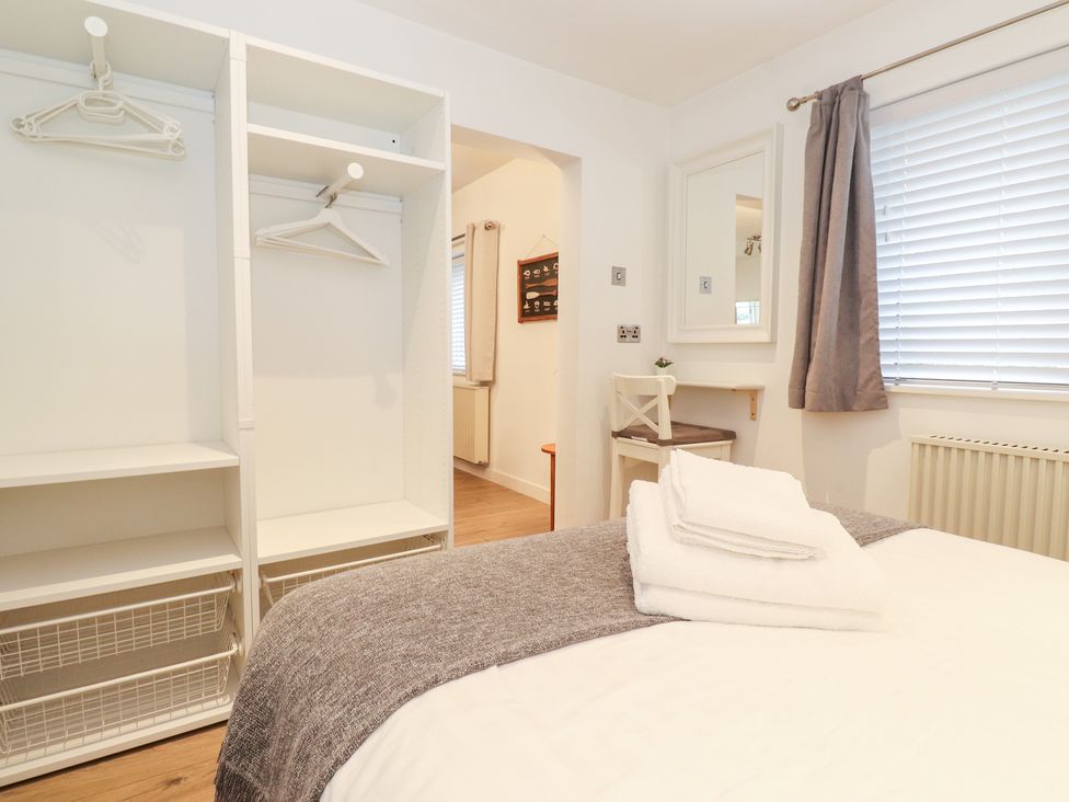 A bedroom with a bed with folded towels a small desk and chair an open wardrobe and a window with blinds and curtains at Canny Cottage Low Hauxley Nr Amble