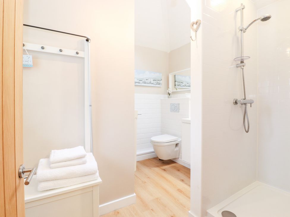 A bathroom with a shower, wall-hung toilet, white towels, and a small cabinet at Canny Cottage Low Hauxley Nr Amble