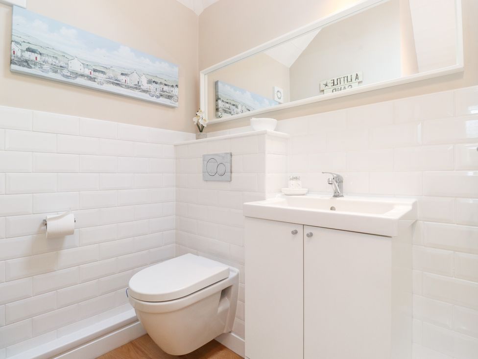 A bathroom with a wall-mounted toilet and a sink with a cabinet and a large mirror at Canny Cottage Low Hauxley Nr Amble