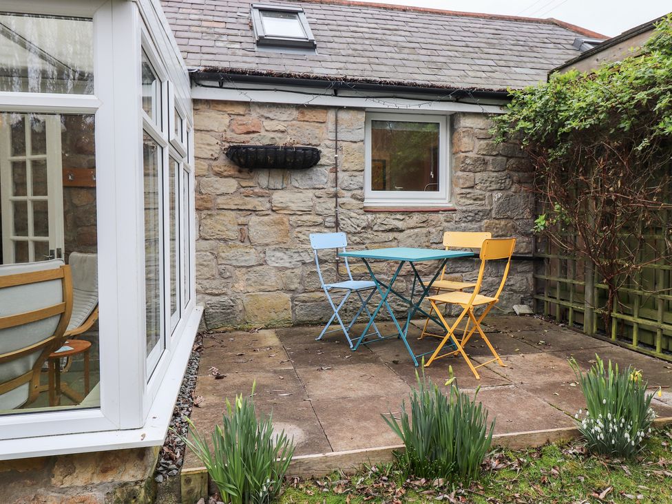 A small outdoor patio with a blue table and two chairs in front of a stone wall at Canny Cottage Low Hauxley Nr Amble