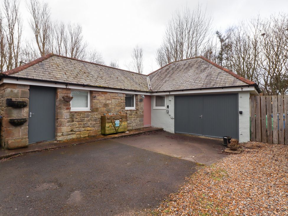 A stone and brick house with a driveway garage and a closed gray door at Canny Cottage Low Hauxley Nr Amble