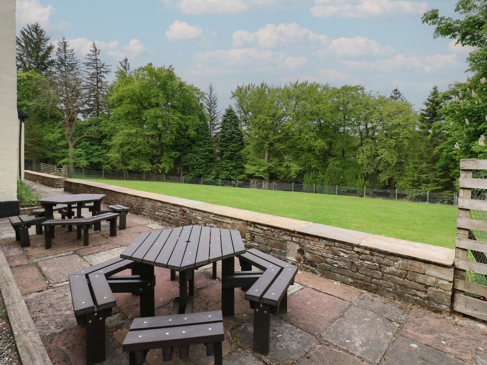 An outdoor patio area with wooden picnic tables and benches next to a grassy lawn and trees at Nenthead House in Nenthead near Alston