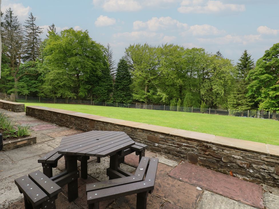 A wooden picnic table with benches on a stone patio facing a lawn and trees at Nenthead House in Nenthead near Alston