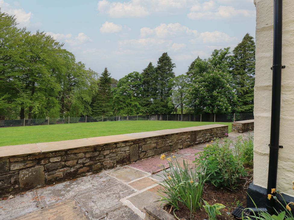 A stone patio with flowerbeds and a grass lawn bordered by a low stone wall and trees at Nenthead House in Nenthead near Alston