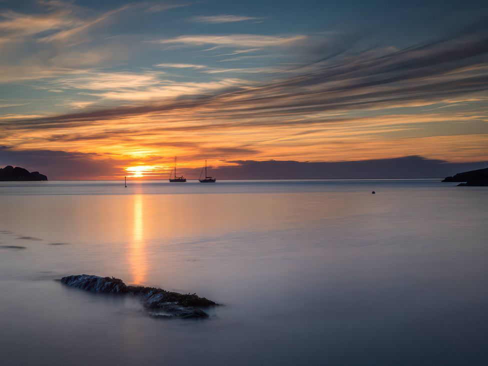 A sunset over the ocean with boats on the water and a rock in the foreground at 2 Manleigh Park Combe Martin