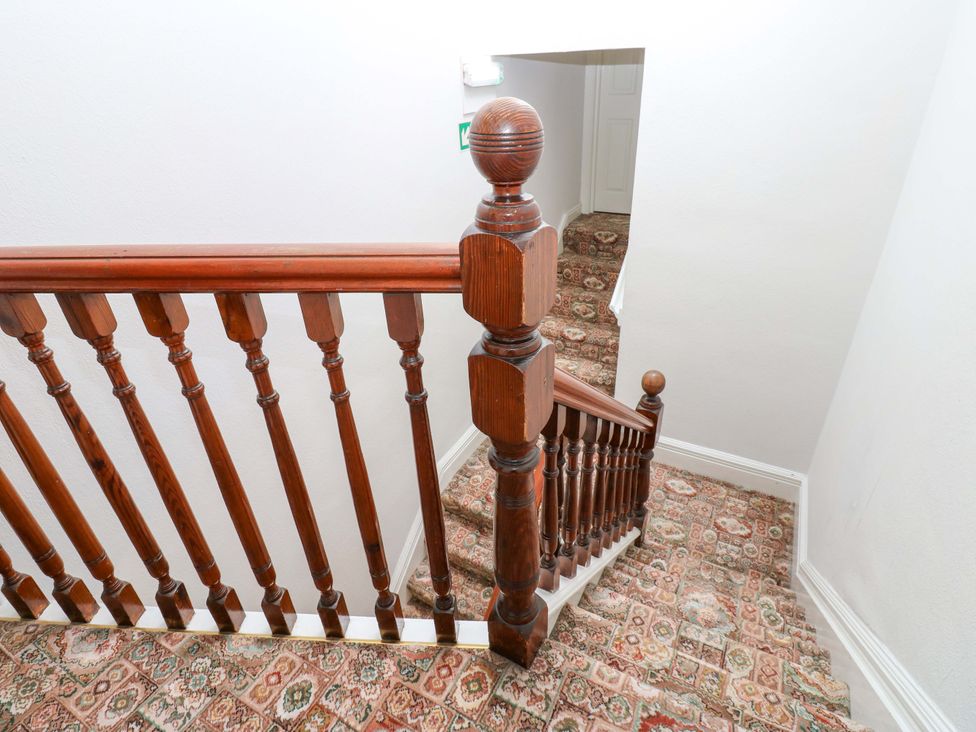 A staircase with a wooden banister and patterned carpet at Fern Lee in Carlisle