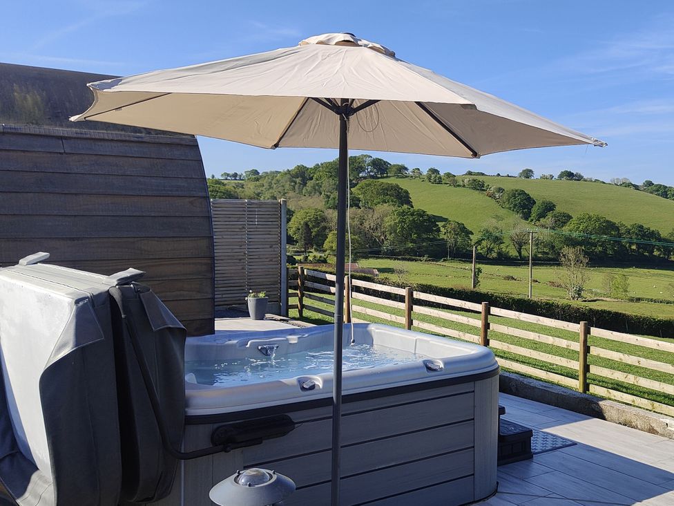A hot tub with an umbrella on a deck at Ceunant in Llanfihangel-y-Creuddyn near Aberystwyth